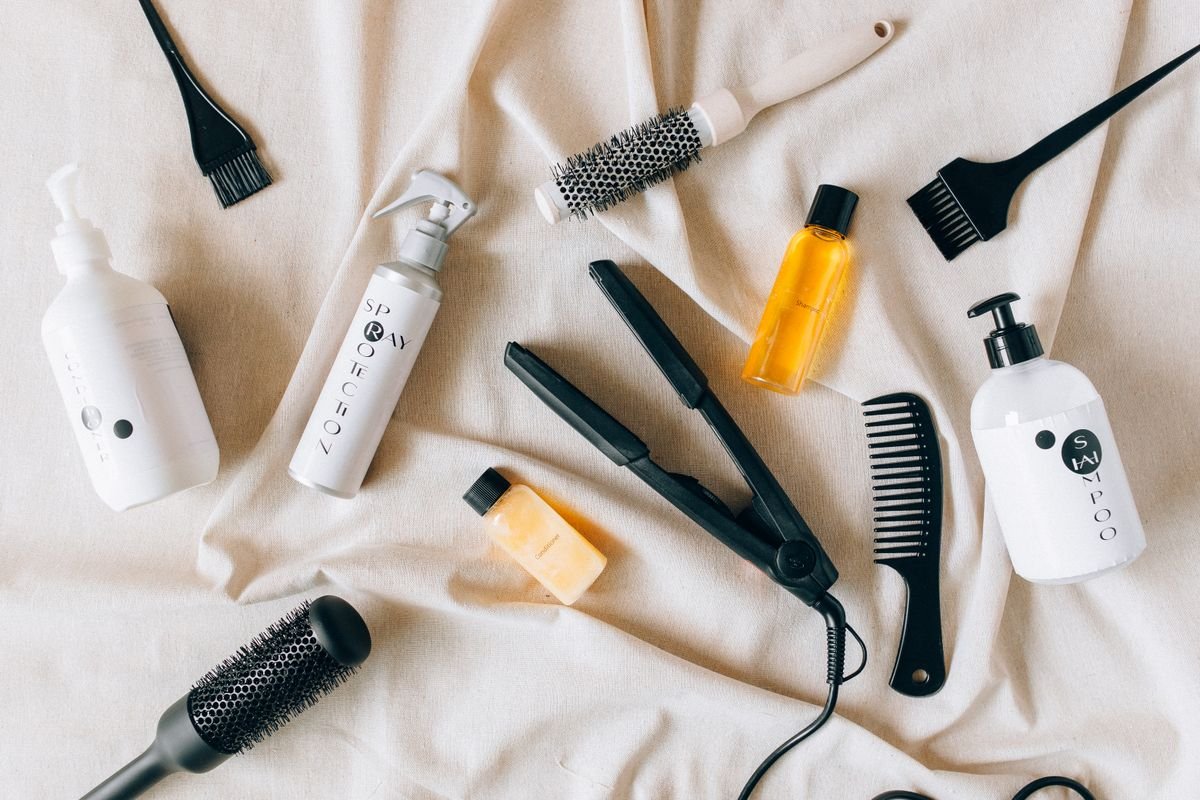 Flat lay of hair care products including shampoo, conditioner, oil, and a comb