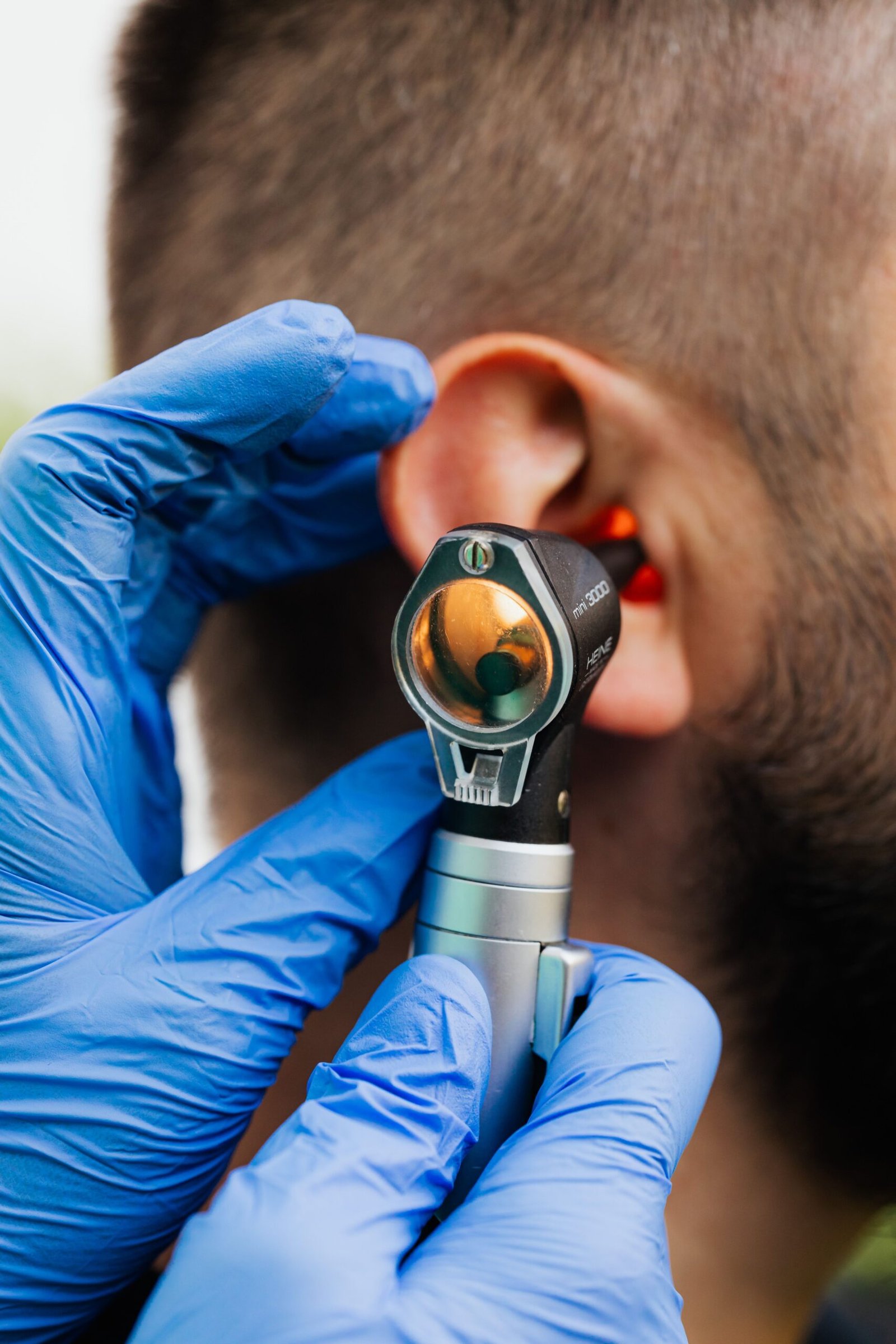 clinician in gloves examining a patient ear with an otoscope