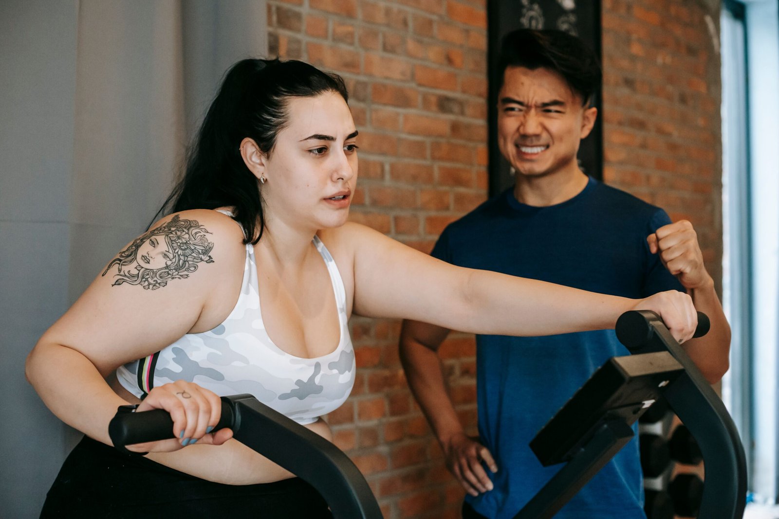 woman training on an elliptical machine with support from a trainer