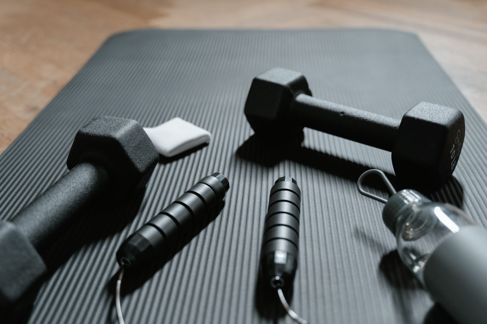 dumbbells, jump rope, and water bottle on a yoga mat