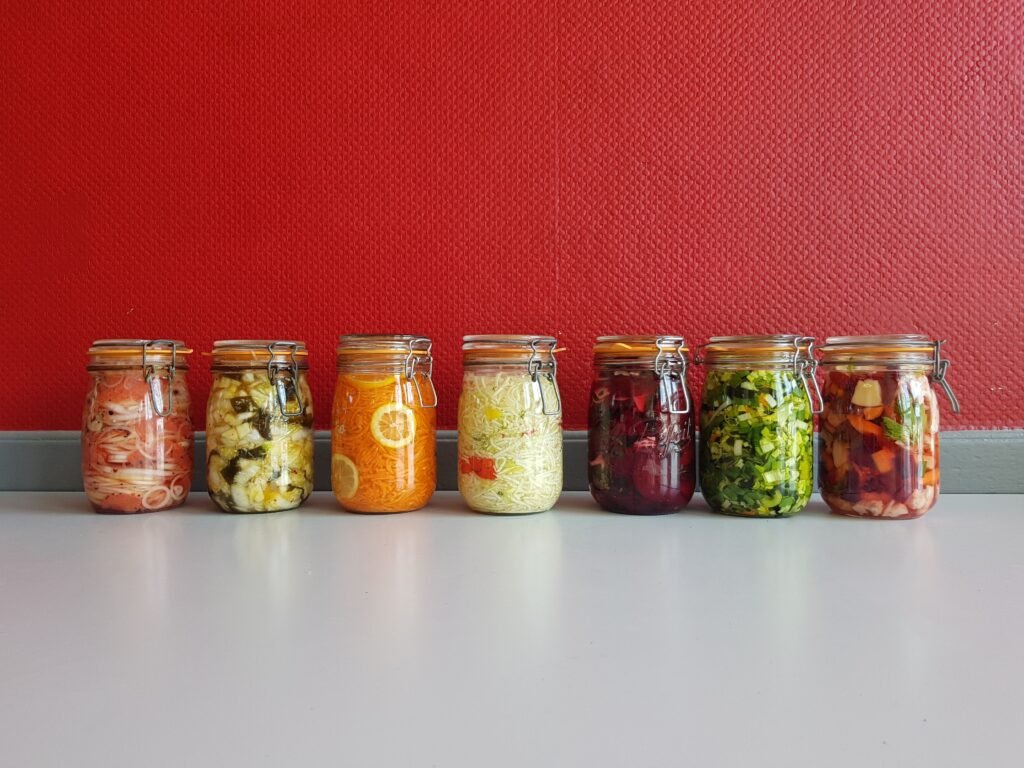 Colorful jars of fermented vegetables, examples of probiotic rich foods, lined up against a wall