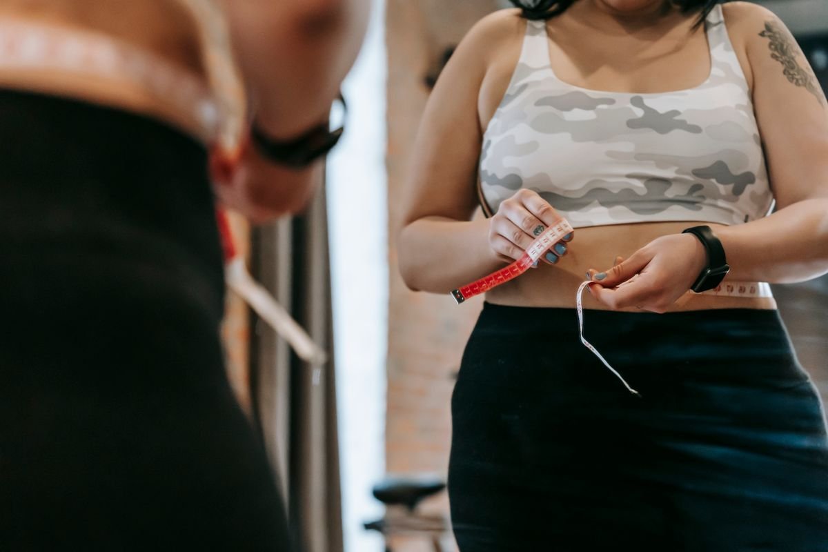Woman measuring her waist with a tape measure to track fitness progress